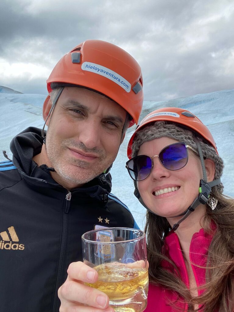 White man and women, Madeleine and Juan Pablo on the Perito Moreno Glacier. Madeleine has a glass of whisky in her hand